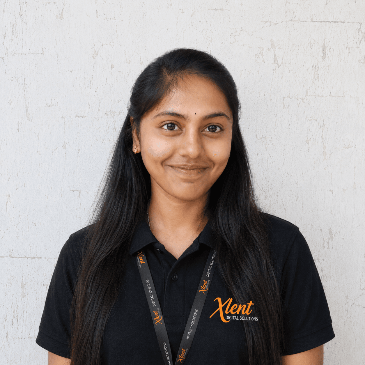 Madhavi Smiling young woman with long black hair in a black polo shirt, wearing an Xlent Digital Solutions lanyard.