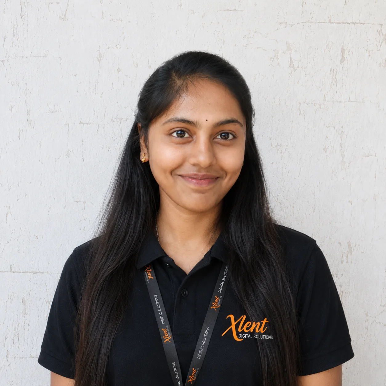 Smiling young woman with long black hair in a black polo shirt, wearing an Xlent Digital Solutions lanyard.